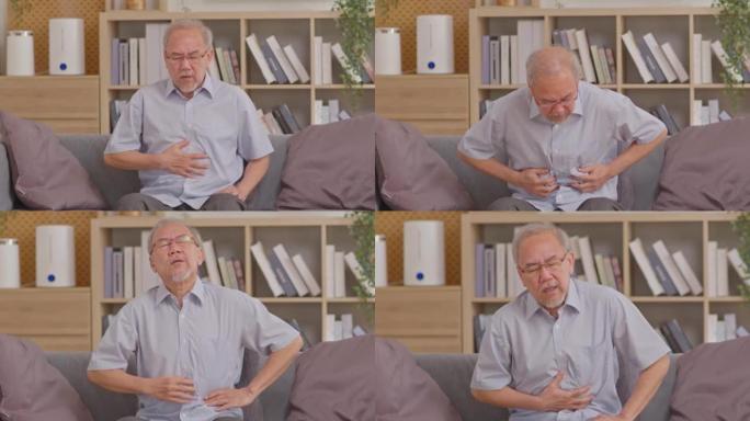 老人坐在家里的沙发上，抱着肚子感到疼痛。亚洲男子胃痛，胃孤立。患有消化问题或胃酸倒流的老年人。