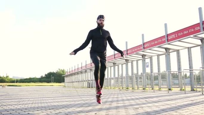 穿着运动服的英俊活泼的年轻大胡子家伙在体育场的特殊覆盖物上锻炼时跳绳跳