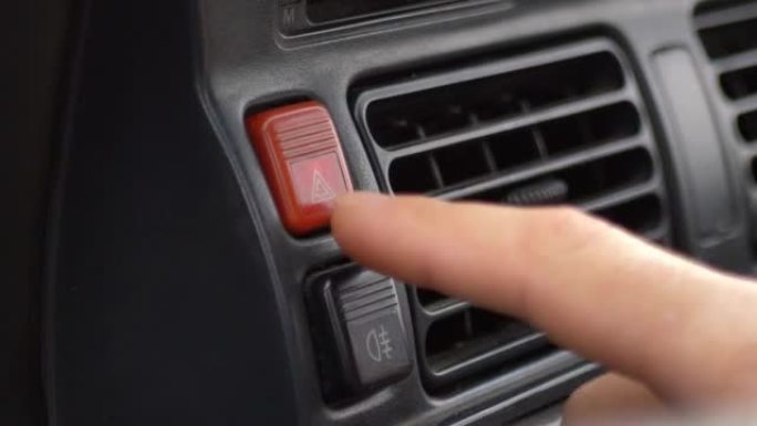一名男子将手指按在面板上的汽车应急照明按钮上。在路上寻求帮助。车辆故障通知。自动紧急按钮