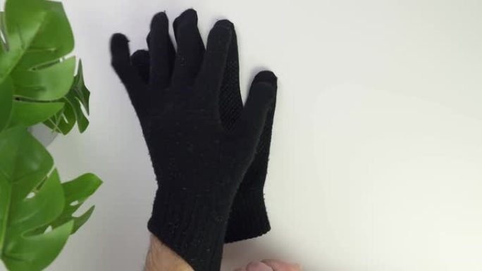 白色背景上的黑色手套俯视图。男性高加索人的手将黑色手套戴在手上。保护皮肤免受寒冷。