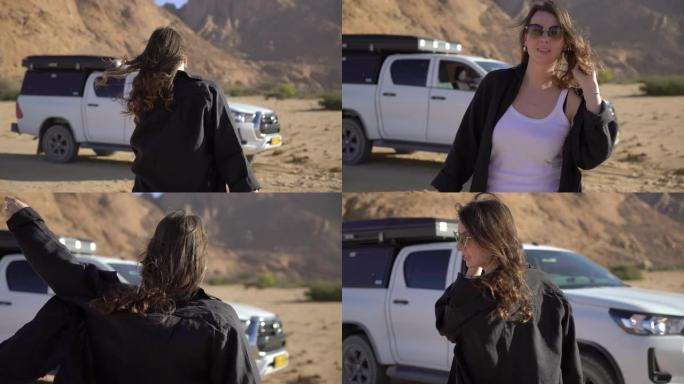 戴着帽子的年轻女子在沙漠中走向她的车。越野车越野汽车