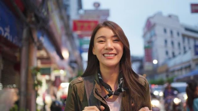 亚洲迷人女性背包客的肖像晚上在城市旅行。年轻女性旅游旅行者站在美丽的街道上，享受在泰国度假旅行的时间