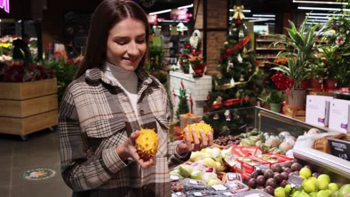 开朗的女人在超市选择异国情调的kiwano水果。杂货店水果部门的女孩