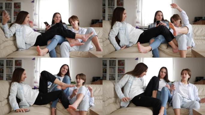 十几岁的女孩三胞胎姐妹在家看智能手机有趣的腿在沙发上打架