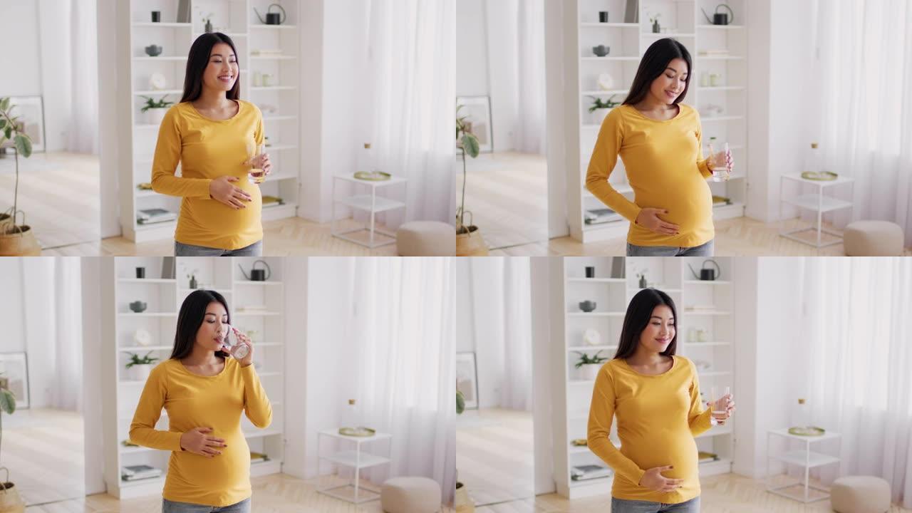 身体水合作用。年轻的亚洲孕妇在家中用玻璃杯喝水