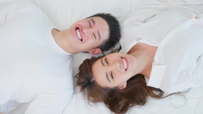 亚洲新婚夫妇躺在床上看着相机的肖像。穿着睡衣的迷人美丽的年轻男女在家里的卧室里享受清晨的活动。家庭关
