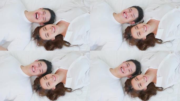 亚洲新婚夫妇躺在床上看着相机的肖像。穿着睡衣的迷人美丽的年轻男女在家里的卧室里享受清晨的活动。家庭关