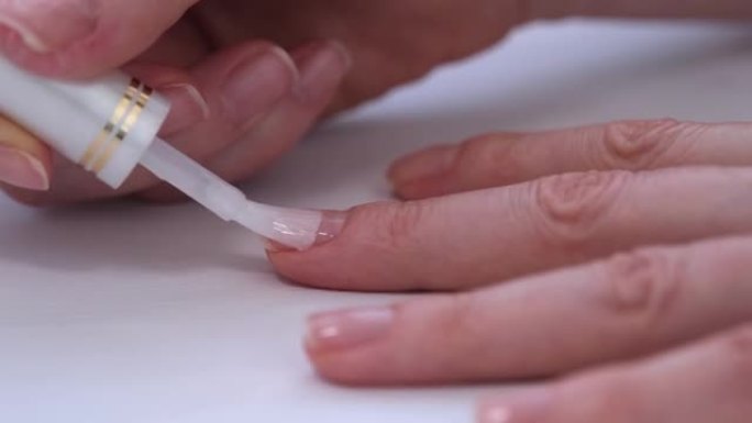 女人的手靠近。这个女孩用透明的医用清漆覆盖指甲。天然美甲。指甲护理。在治疗剂的帮助下加强指甲