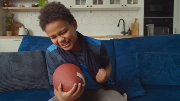 兴奋可爱的黑人男孩在电视上观看美式足球，庆祝达阵