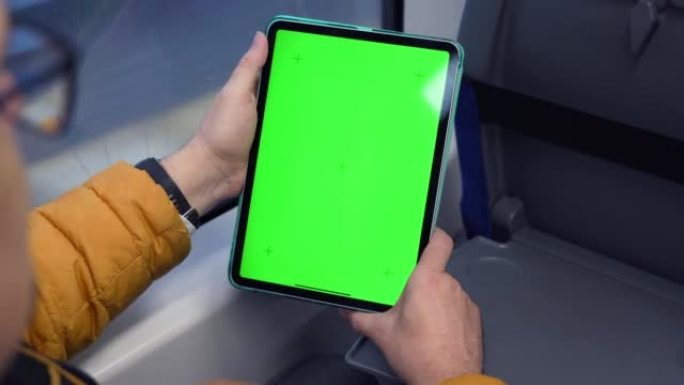 绿屏和火车在线浏览的man watch平板电脑的后视图。模拟观看pad上的内容。坐在公共交通工具室内