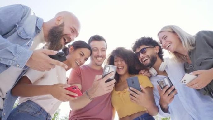 多种族快乐的朋友使用电话并在外面一起微笑的低角度。人们沉迷于技术和社交媒体