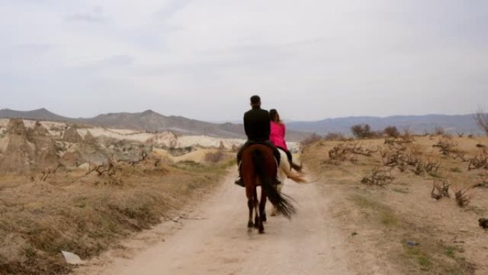 无法识别的骑手在荒凉的风景中骑着三匹马。三个朋友在大风天在土耳其卡帕多西亚的山和岩石上骑马。