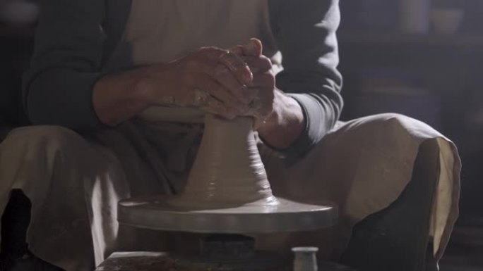 陶工的男性双手塑造并雕刻了柔软的白色陶罐，在创意车间的陶工轮上旋转。师父给陶器赋予了不同的形状。粘土