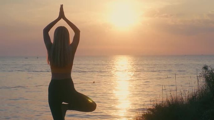 女人在夏天的日落中有海洋背景在做瑜伽。热身，健康生活，放松和户外运动。保健，真实性，平衡感和镇定感。