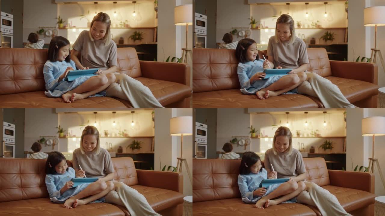充满爱心的亚洲妈妈和小女儿一起坐在家里的沙发上，平板电脑设备用铅笔绘制，使用教育应用程序轻松有趣地学