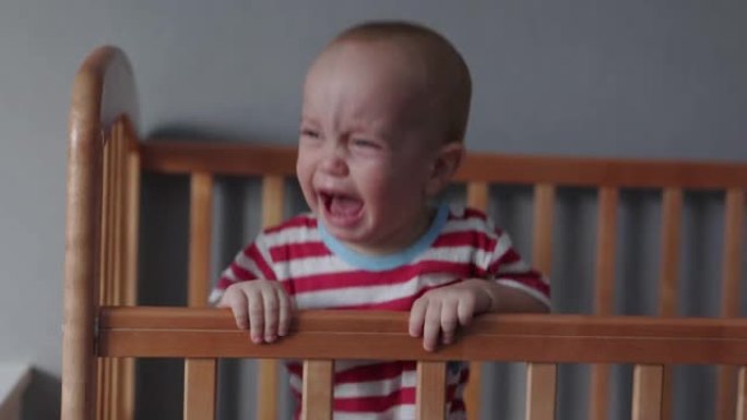 哭泣的小孩站在婴儿床床上尖叫，伸出双手