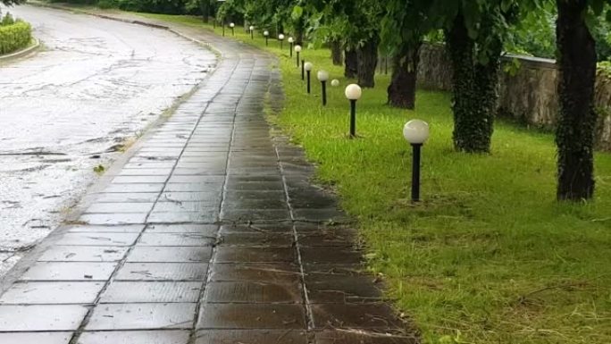 4k视频，人行道上的混凝土板被雨水弄湿，在城市公园阴雨多雨的夏日，沿着小巷的灯笼和树木，相机变焦