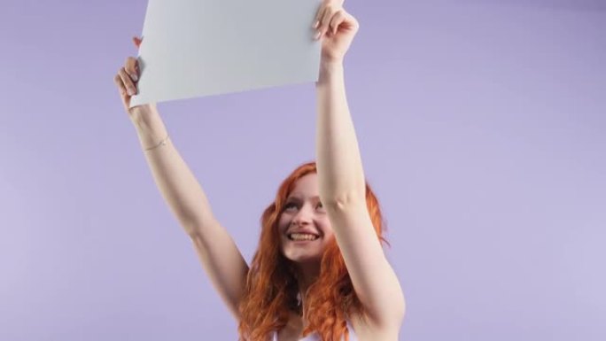 兴奋的红发女人保持纸张复印空间，用于广告产品服务隔离在紫色工作室背景。
