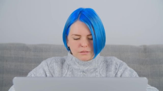 专注的自由职业者女性在现代笔记本电脑上打字文本。抄写员在网上做远程工作。在电脑上工作的染蓝头发的创意
