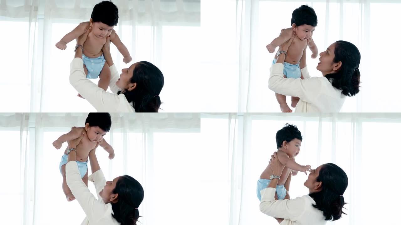 4K 50fps，亚洲单身妈妈和刚出生的儿子在卧室玩。她抬起儿子，假装高兴而有趣地在空中飞翔。概念幸