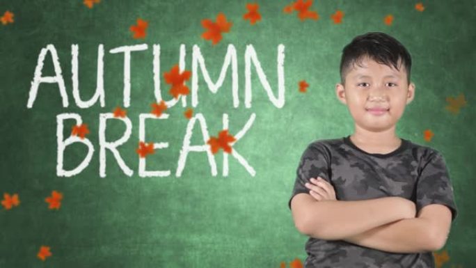 男小学生站在教室里，用黑板上的秋假文字竖起大拇指