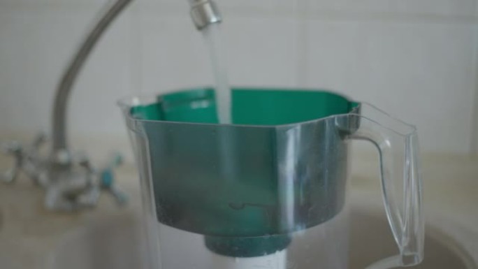 水槽中的过滤水壶，水龙头内倒水。厨房室内碳净化设备特写。