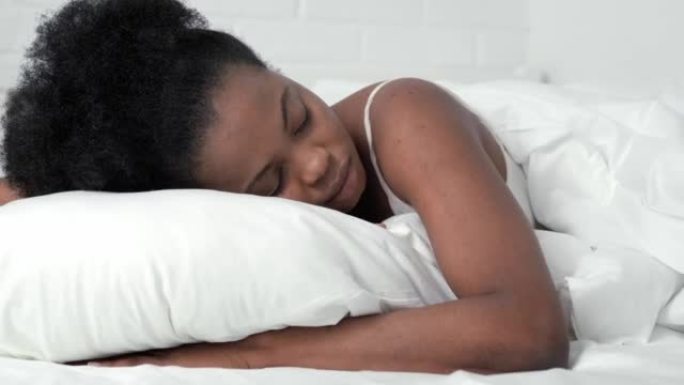 安详的非洲裔美国妇女睡在舒适的床上，躺在柔软的枕头矫形床垫上，平静的年轻黑人女士躺在卧室的白色床单上