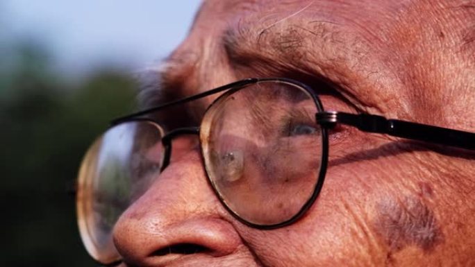 戴眼镜的老人的特写脸在阳光下向远处望去。愿景与老年人观念