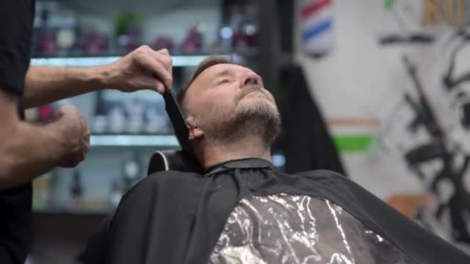 理发师在沙龙用电动剃须刀剃英俊成熟的大胡子男人。美发艺术家在男性理发店为人们制作胡须风格。专业造型师