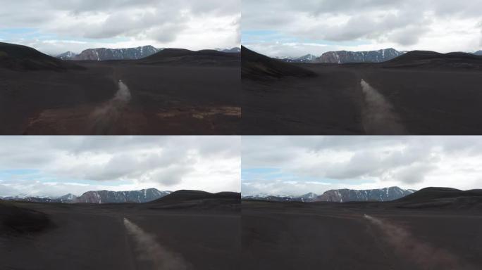 快速移动和除尘的汽车经过贫瘠的平原和火山灰的高镜头。背景中的山脊。冰岛
