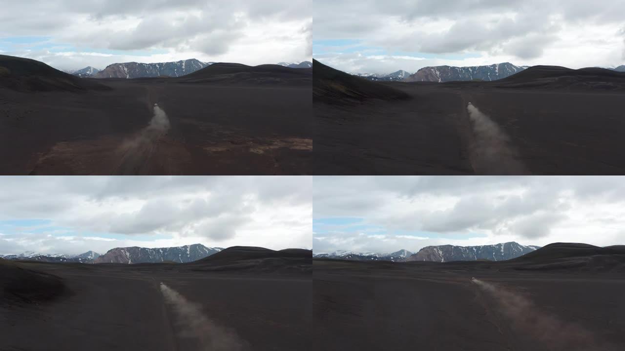 快速移动和除尘的汽车经过贫瘠的平原和火山灰的高镜头。背景中的山脊。冰岛