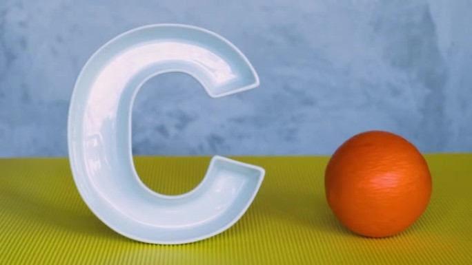 食物中的维生素c，threpsology概念。灰色和黄色背景上的字母C形状的盘子，人的手将新鲜的橙色