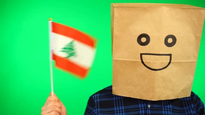 男人的肖像与纸袋在头上挥舞黎巴嫩国旗与微笑的脸在绿色的背景。