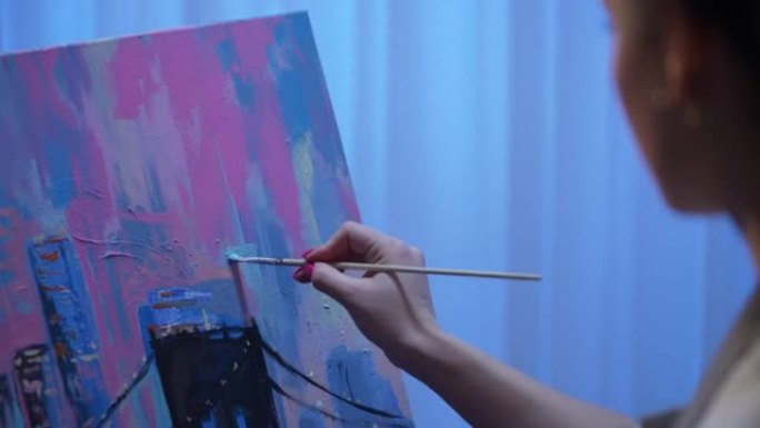 从创意工作室的画布上艺术家绘画的背面看。年轻女子用画笔和调色板上的油画创作绘画。建筑物关闭的城市。慢