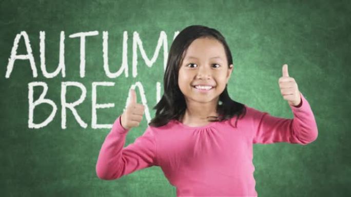 小女孩竖起大拇指，黑板上写着秋假的文字，在教室里拍摄