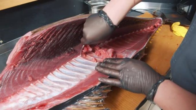 市场上金枪鱼切割过程的特写。男人戴着手套的手从里面清洗一条大鱼。