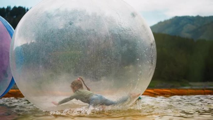 女孩爬进漂浮在公园池塘里的水球里