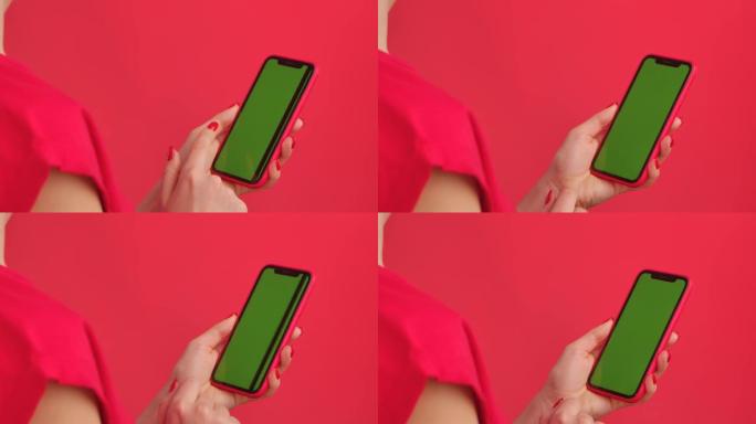女人拿着红色工作室背景上的绿色工作区模拟屏幕的手机。女性手触摸、点击、滑动。广告区域。模板位置。特写