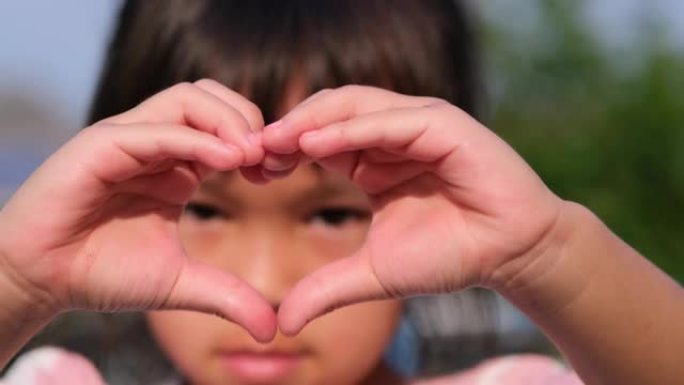 一个亚洲小女孩看着相机，用手做心形的特写镜头。爱的心象征。