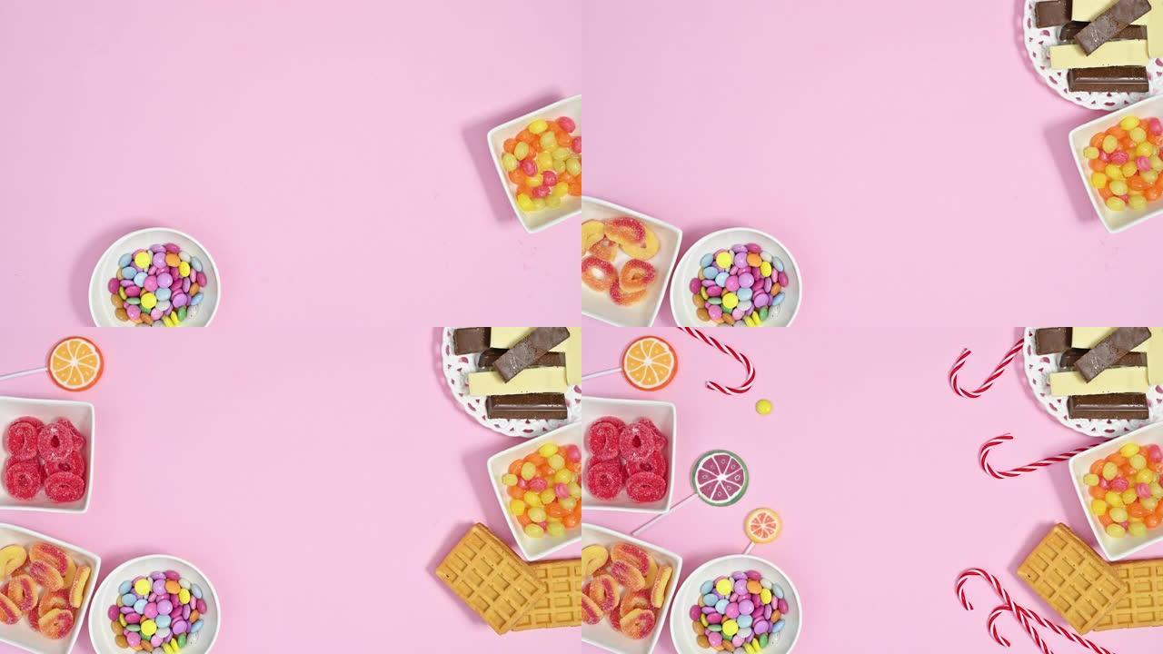 甜品糖果，巧克力，棒棒糖和软糖糖果填充碗在柔和的粉红色背景的左侧和右侧。停止运动动画平躺