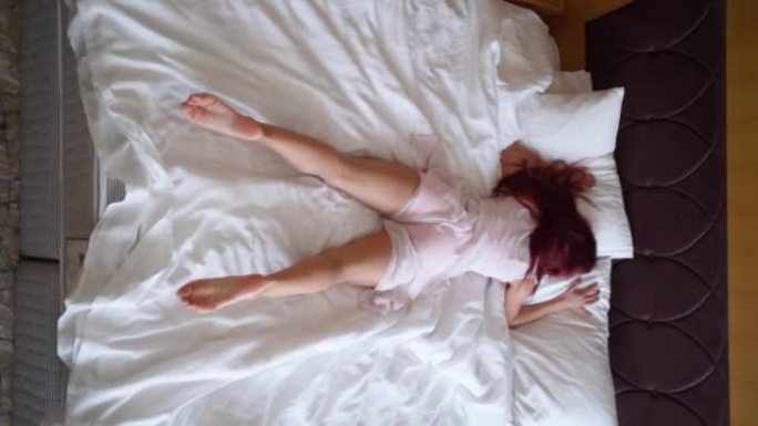 疲倦的女人跳上床，休息和睡觉。垂直视频。慢动作