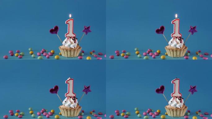 祝1岁宝宝生日快乐，带蜡烛的生日蛋糕和蓝色背景上的生日装饰品。复制空间