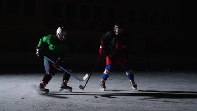 两名身穿制服和头盔的男子在冰场上滑冰，碰撞，运球并击中冰球。职业曲棍球运动员在带有聚光灯的黑暗溜冰场