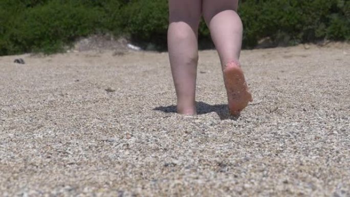 脚女人在砾石海滩上行走，它湿着脚，走路时摔倒