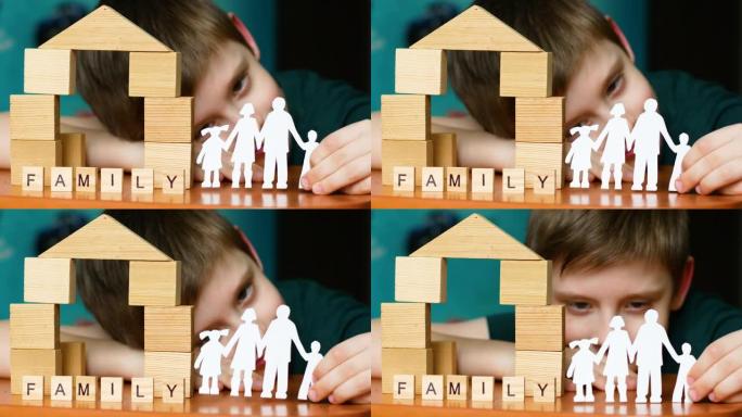 一个6-7岁的高加索男孩手里拿着一个家庭的剪纸剪影。木字家族的题词，木块在房子里的儿童游戏。选择性聚