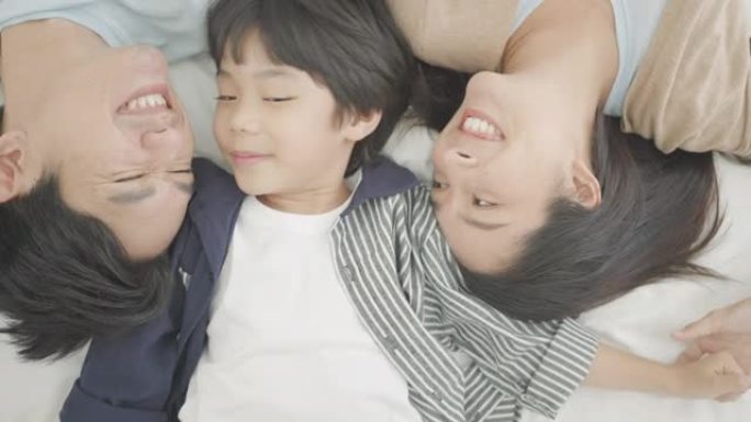 顶视图。快乐的亚洲家庭在舒适的家里，爸爸妈妈和可爱的儿子玩耍，在休闲的卧室里一起在舒适的床上笑着放松