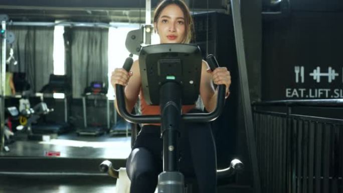 亚洲美女年轻成年白人妇女在体育俱乐部的自行车机上锻炼。有氧训练概念