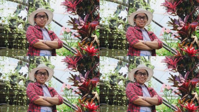一个微笑的园丁女人的肖像，双臂交叉在温室中的花卉植物上站着。在花园工作的年轻女企业家。小企业主的启动