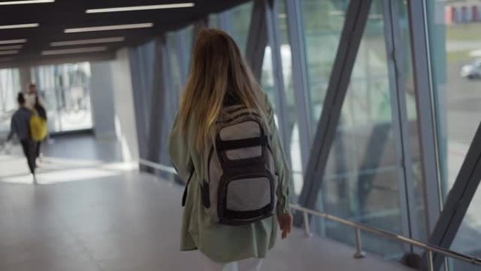 女游客背着背包走到机场航站楼门口的后视