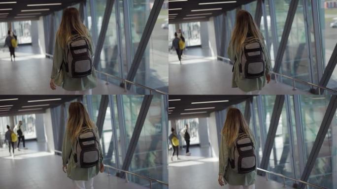 女游客背着背包走到机场航站楼门口的后视